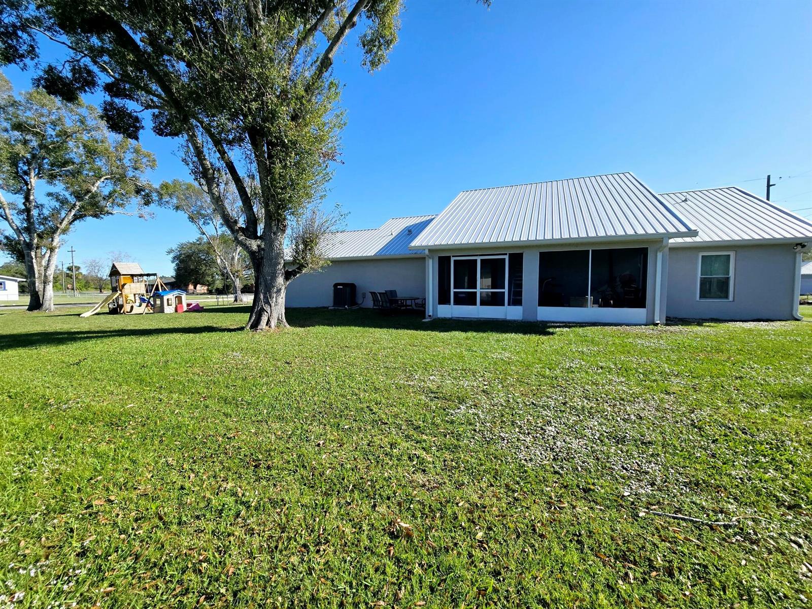 A backyard view of a house with a metal roof, screened porch, and playground equipment — 603 NW 11th Avenue, Okeechobee FL 34972, OKEECHOBEE, FL