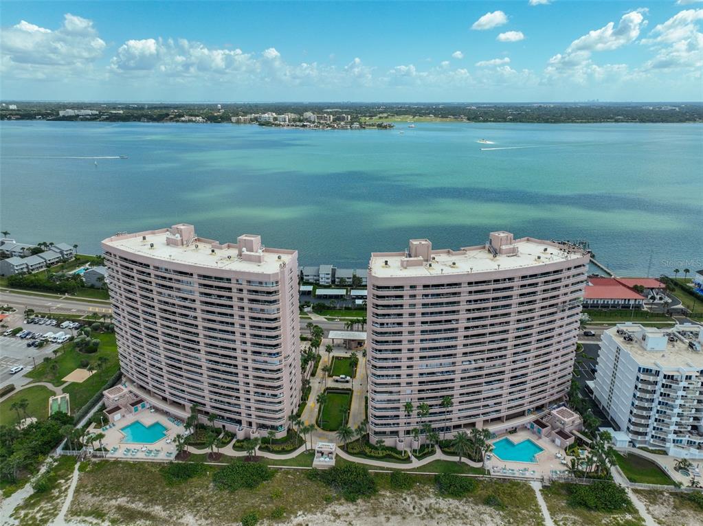 An aerial view of two tall, pink residential towers situated along a sandy beach — 1340 GULF BOULEVARD UNIT 11C, CLEARWATER BEACH, FL