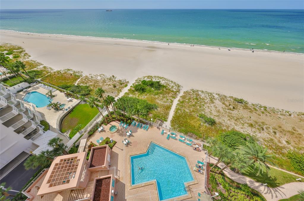 An aerial view shows a beach, a swimming pool, and a multi-story building — 1340 GULF BOULEVARD UNIT 11C, CLEARWATER BEACH, FL