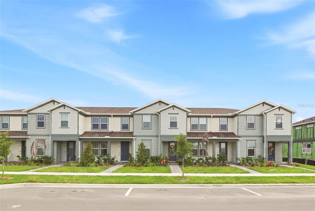 A row of multi-story townhomes with light-colored siding and gabled roofs under a blue sky — 10148 HADLEY STREET, ORLANDO, FL