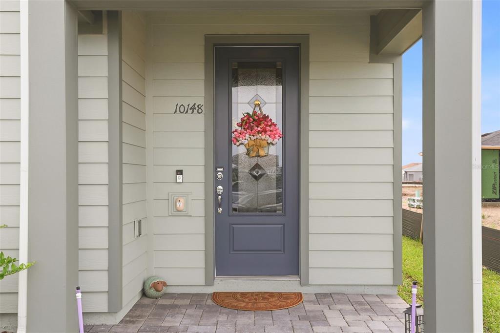A gray front door with a glass insert and floral wreath sits under a porch — 10148 HADLEY STREET, ORLANDO, FL
