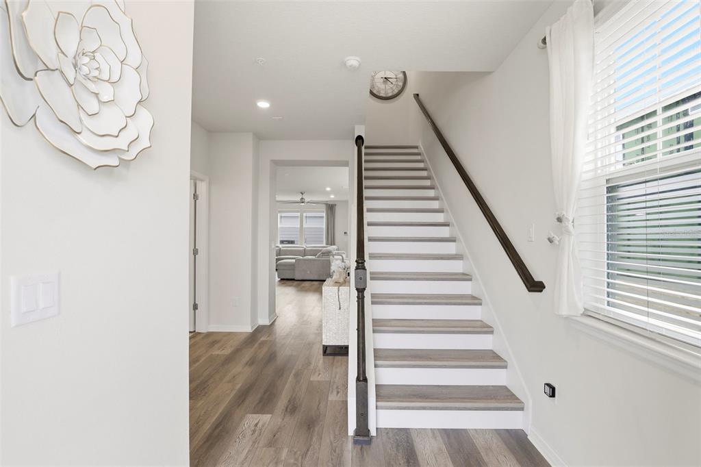 A bright entryway features wood-look flooring, a staircase with a dark railing, and white walls — 10148 HADLEY STREET, ORLANDO, FL