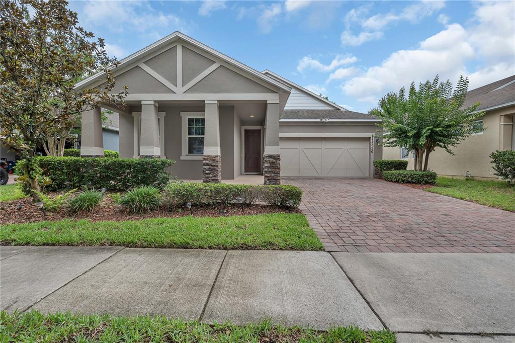 A single-story house with a stone-accented porch, a brick driveway, and a two-car garage — 12826 WOODMERE CLOSE DR, WINDERMERE, FL