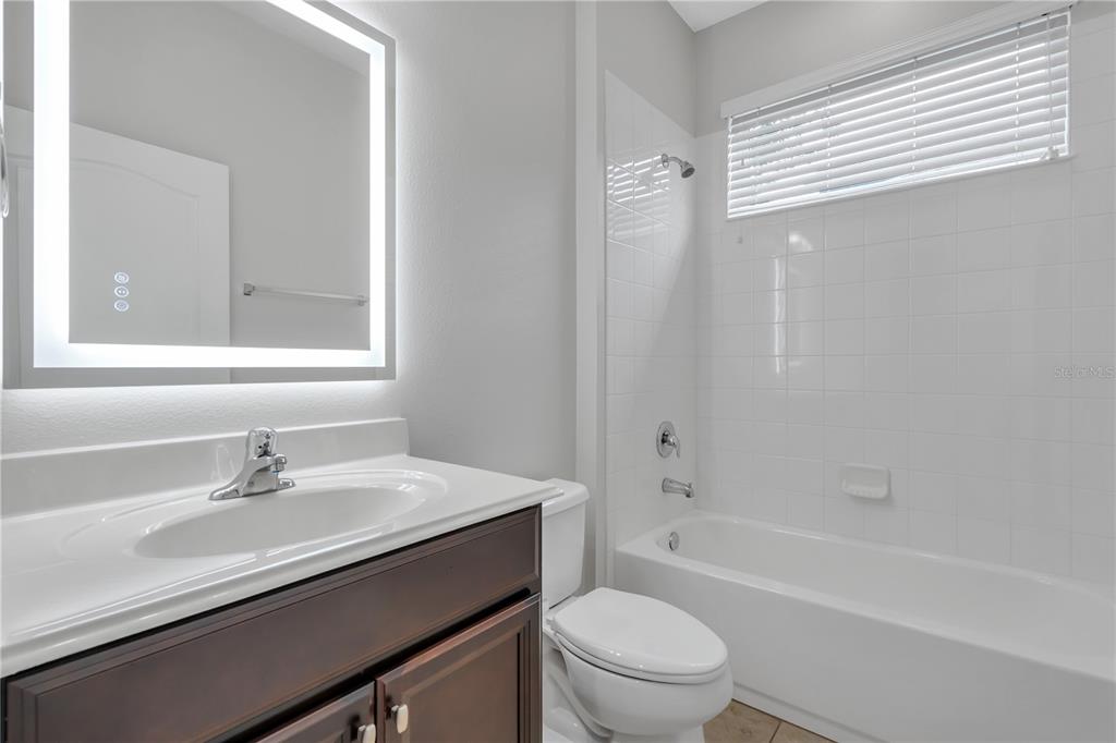 A bathroom features a dark wood vanity, a lighted mirror, and a white tiled tub — 12826 WOODMERE CLOSE DR, WINDERMERE, FL