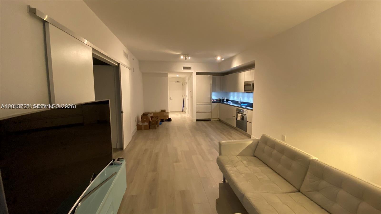This open-concept living area features light wood flooring, a white sofa, and a kitchen — 1010 Brickell Ave # 2208, Miami FL 33131, MIAMI, FL