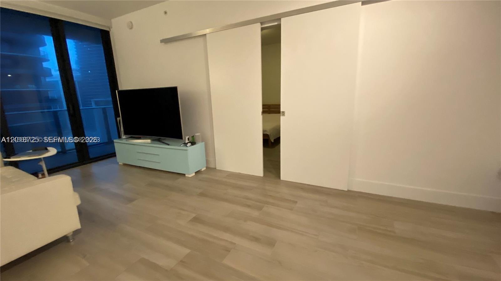 A living room features light wood flooring, a television on a blue console, and sliding doors — 1010 Brickell Ave # 2208, Miami FL 33131, MIAMI, FL