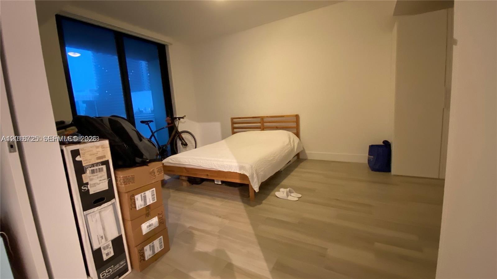 A bedroom features light wood flooring, a bed with a wooden frame, and floor-to-ceiling windows — 1010 Brickell Ave # 2208, Miami FL 33131, MIAMI, FL