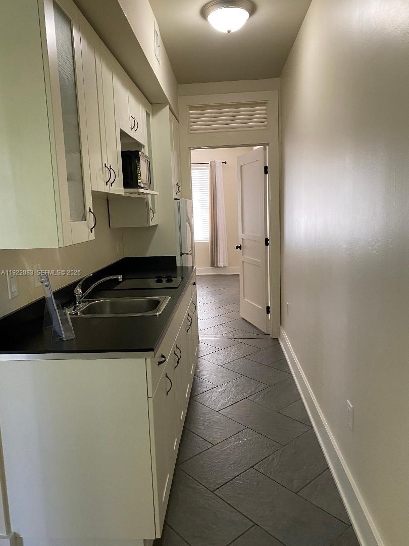 A narrow galley kitchen features white cabinets, black countertops, and dark gray tile flooring — 119 Cibao Ct # 3, Coral Gables FL 33134, CORAL GABLES, FL