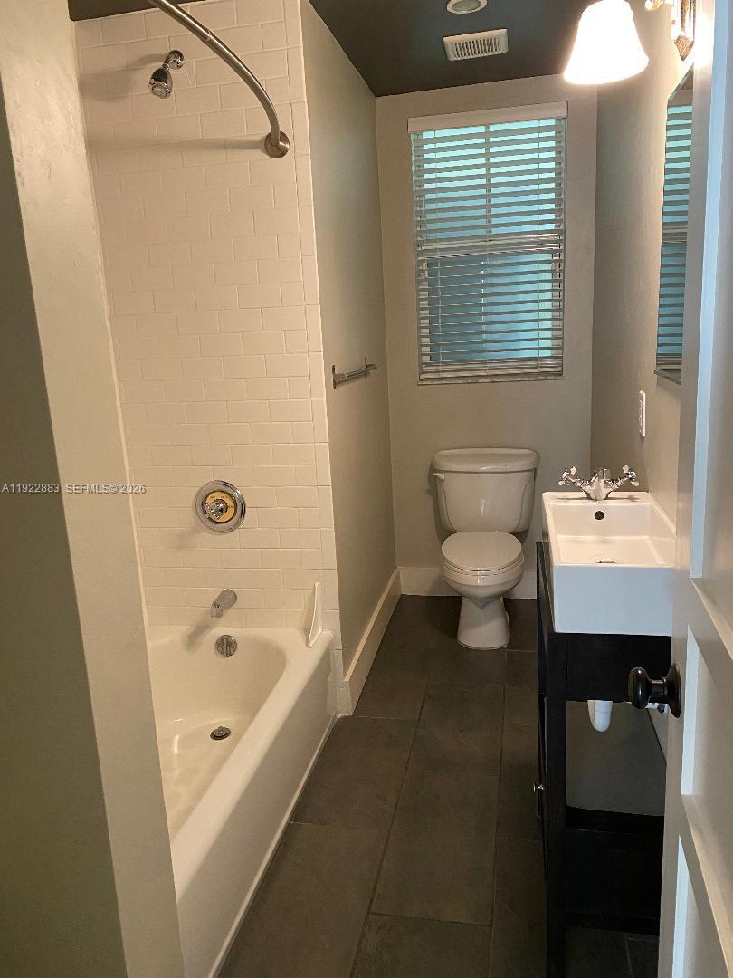 A bathroom features a white subway-tiled shower-tub combo, a pedestal sink, and dark floor tiles — 119 Cibao Ct # 3, Coral Gables FL 33134, CORAL GABLES, FL