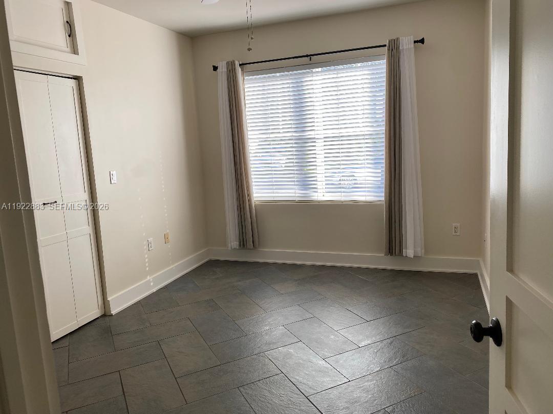 A bedroom with gray tile flooring, a window with blinds, and a white closet — 119 Cibao Ct # 3, Coral Gables FL 33134, CORAL GABLES, FL