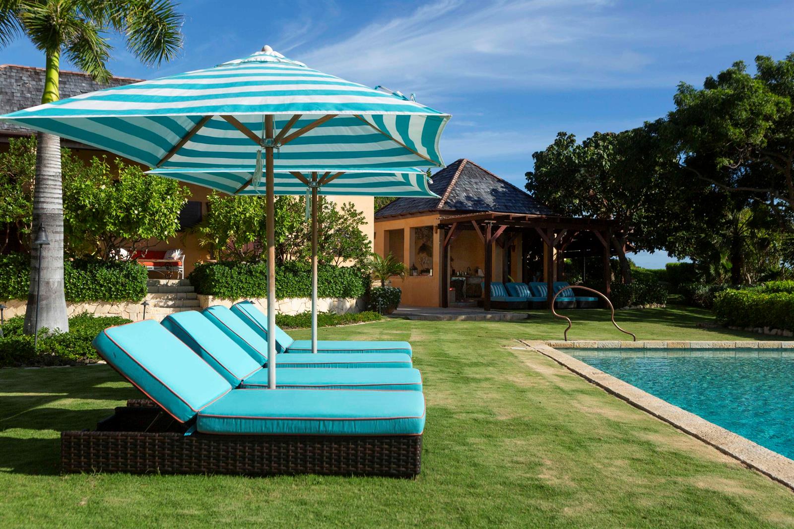 Turquoise lounge chairs sit under striped umbrellas on a grassy lawn beside a swimming pool — 0 Pelican Ridge, FL