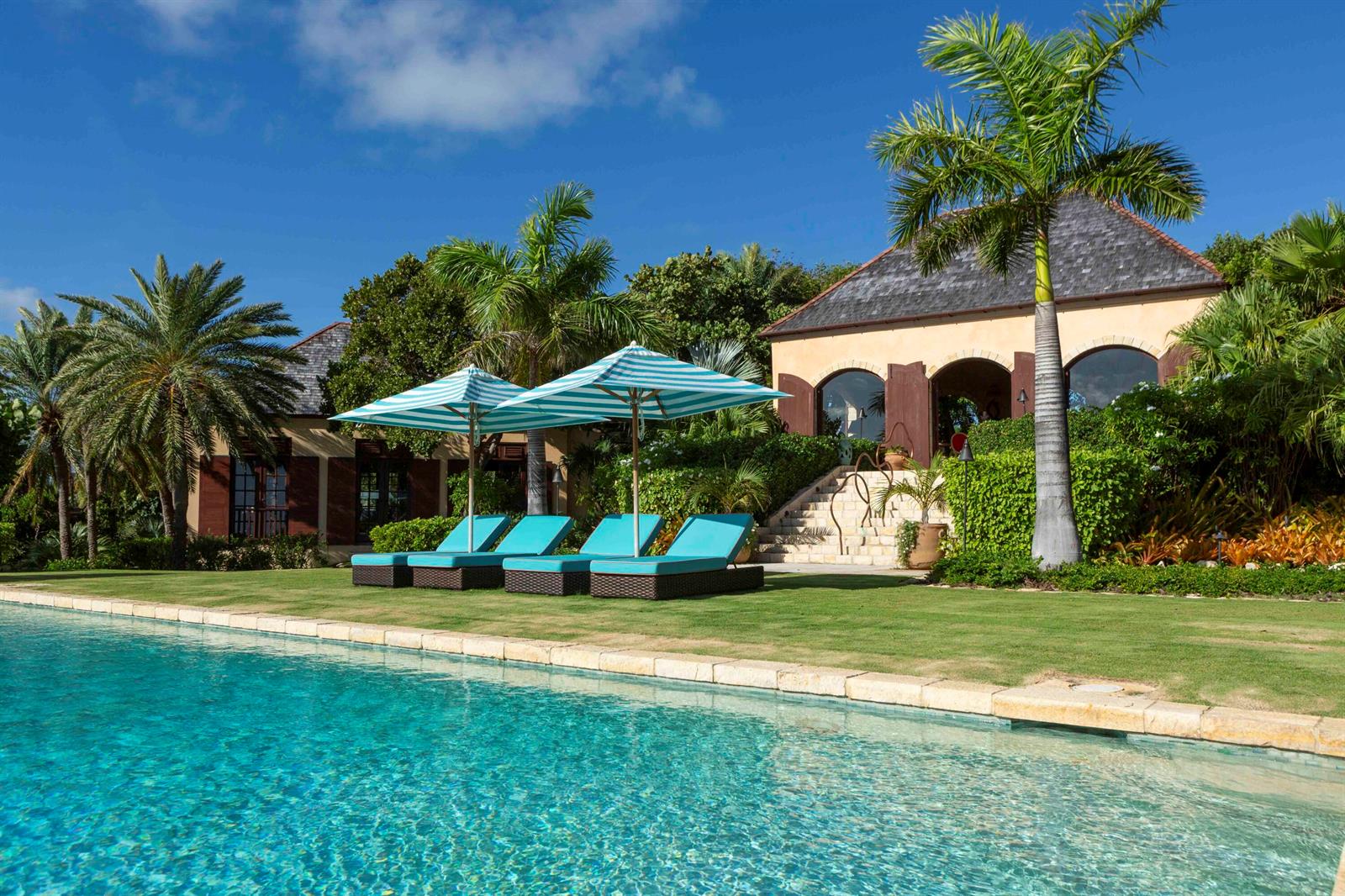 A swimming pool sits in front of lounge chairs, umbrellas, and a villa with landscaping — 0 Pelican Ridge, FL