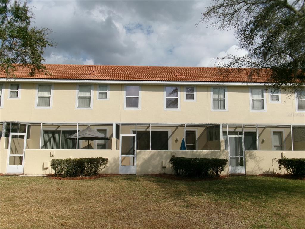 The exterior of a multi-unit townhouse features a tiled roof, beige stucco walls, and screened-in patios — 1285 S SOUTH BEACH CIRCLE CIRCLE, KISSIMMEE, FL