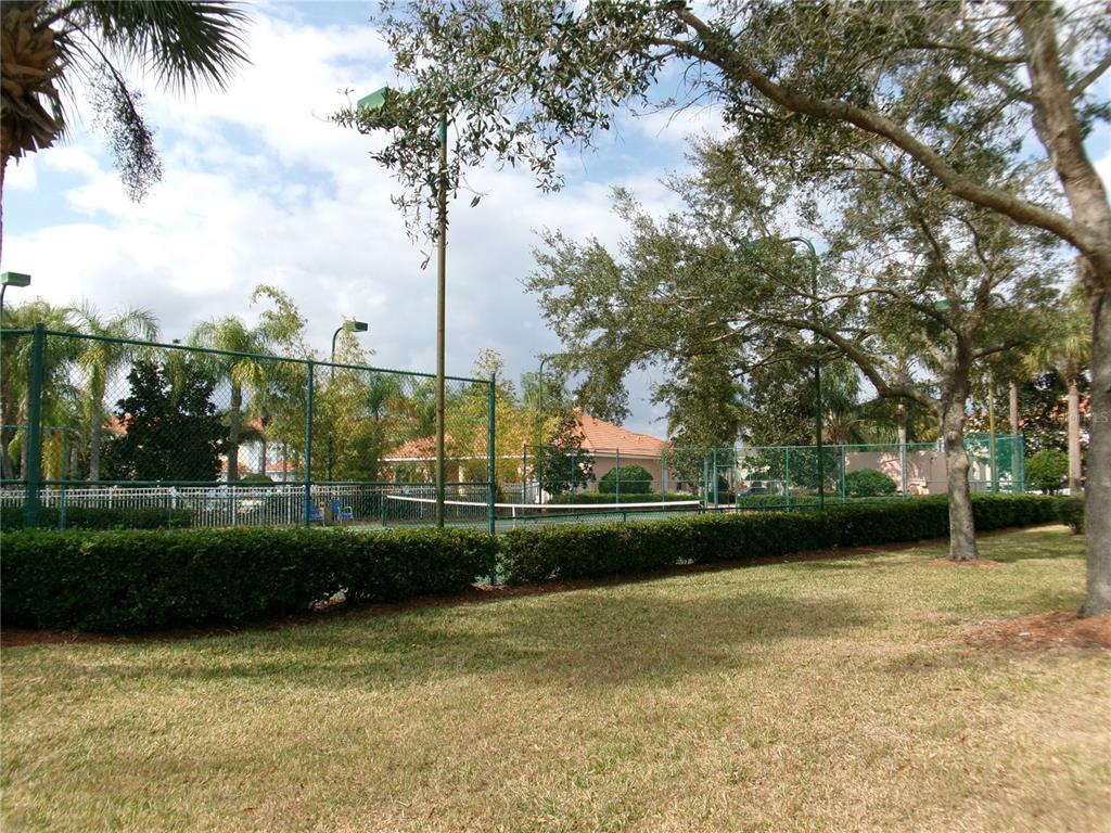 A fenced tennis court is surrounded by manicured hedges and trees on a sunny day — 1285 S SOUTH BEACH CIRCLE CIRCLE, KISSIMMEE, FL