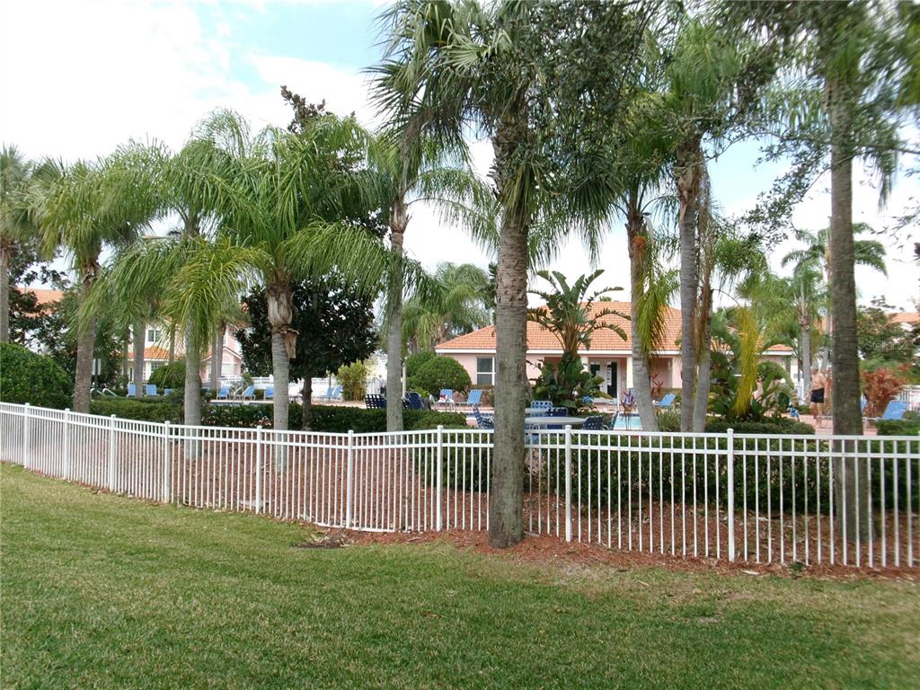 A white metal fence surrounds a swimming pool area with palm trees and a clubhouse — 1285 S SOUTH BEACH CIRCLE CIRCLE, KISSIMMEE, FL