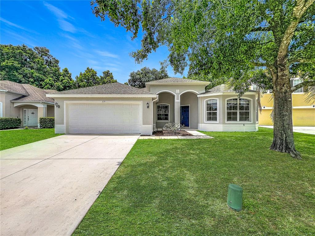 A single-story house with a two-car garage, a blue front door, and a large tree — 235 MAGNOLIA PARK TRAIL, SANFORD, FL