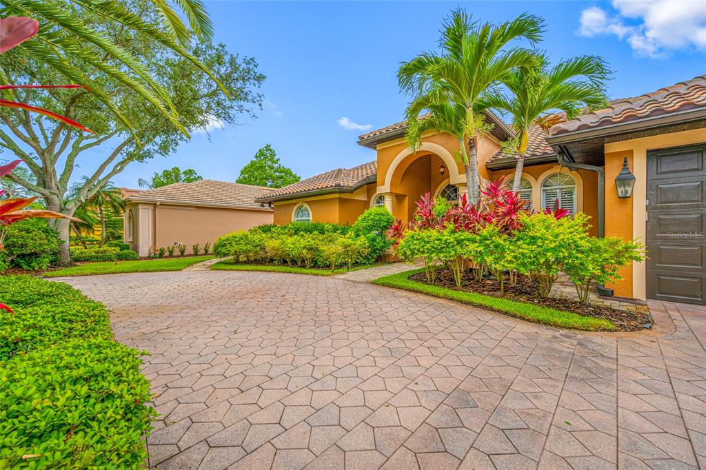 A paved driveway leads to the entrance of a tan house with palm trees — 7888 BAYOU CLUB BOULEVARD, SEMINOLE, FL