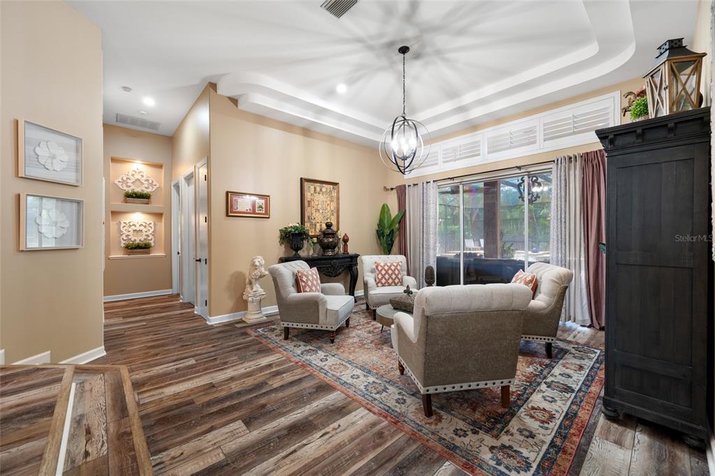 A living room features wood-look flooring, a tray ceiling, a chandelier, and three upholstered chairs — 7888 BAYOU CLUB BOULEVARD, SEMINOLE, FL