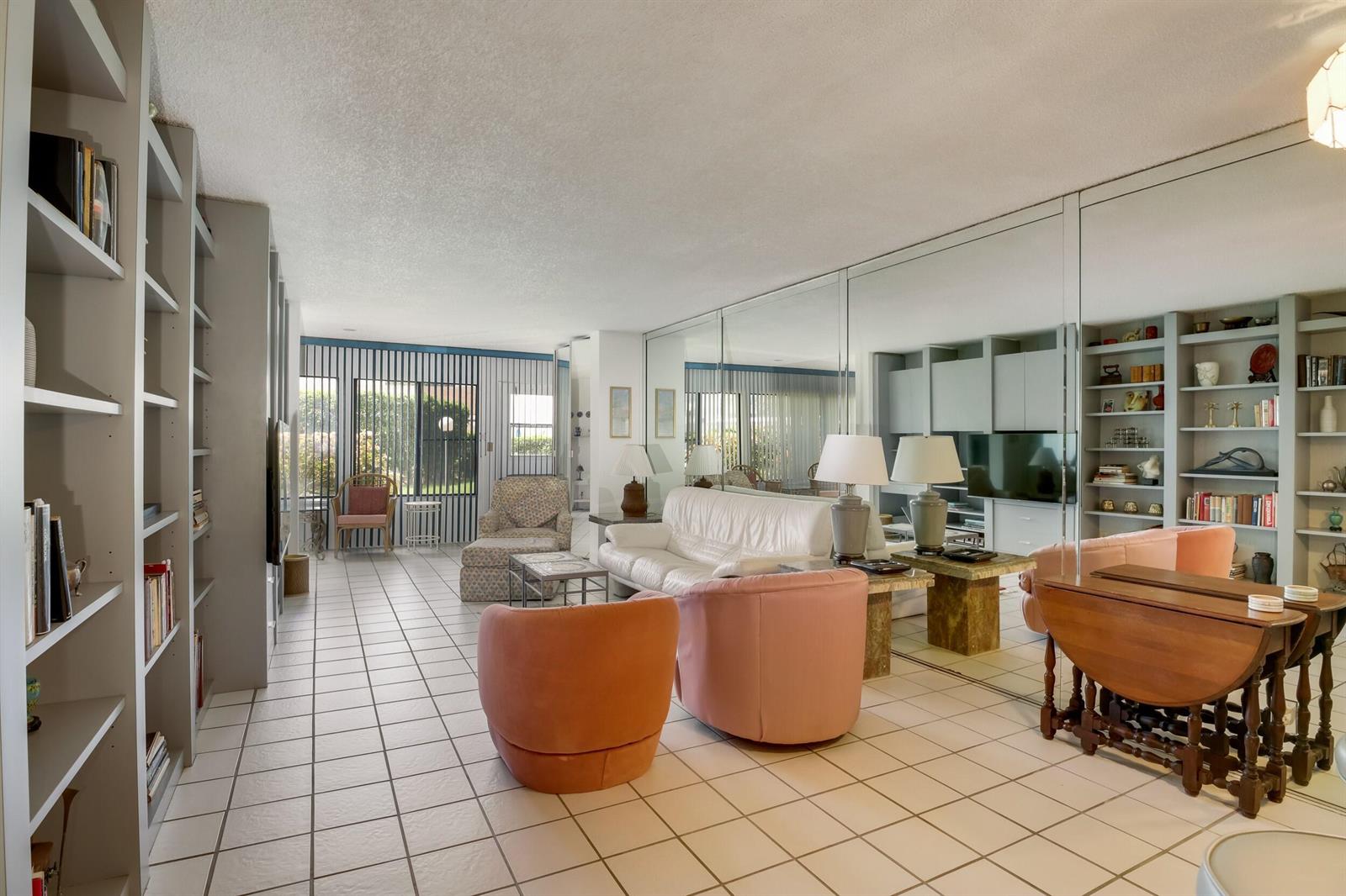 A living room features white tile floors, built-in shelving, a mirrored wall, and pink armchairs — 3154 Via Poinciana # 116, FL 33467, FL