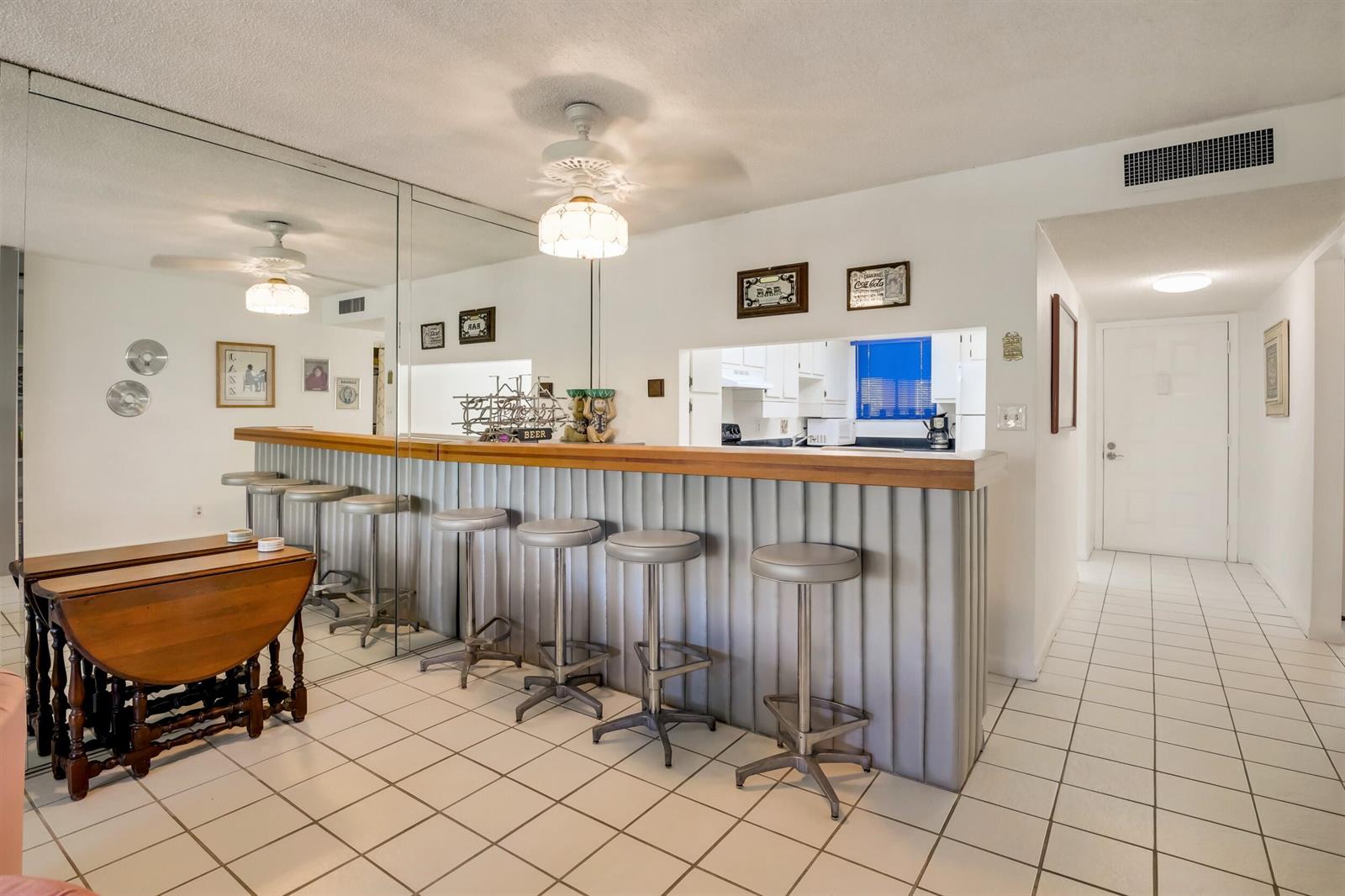 A home bar area features a wooden countertop, gray corrugated base, and several metal stools — 3154 Via Poinciana # 116, FL 33467, FL