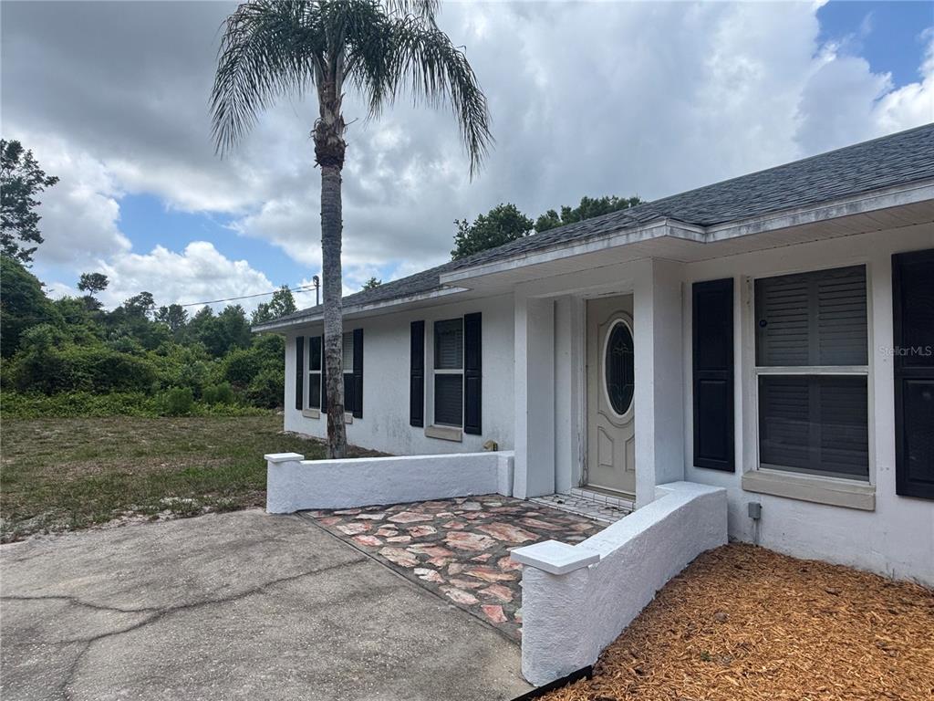 A white house exterior features a stone-paved front porch, black shutters, and a palm tree — 510 S CEDAR AVENUE, ORANGE CITY, FL
