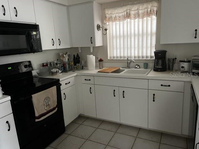A kitchen features white cabinets, black appliances, a tiled floor, and a window with blinds — 8407 OAK JAY LANE, ENGLEWOOD, FL
