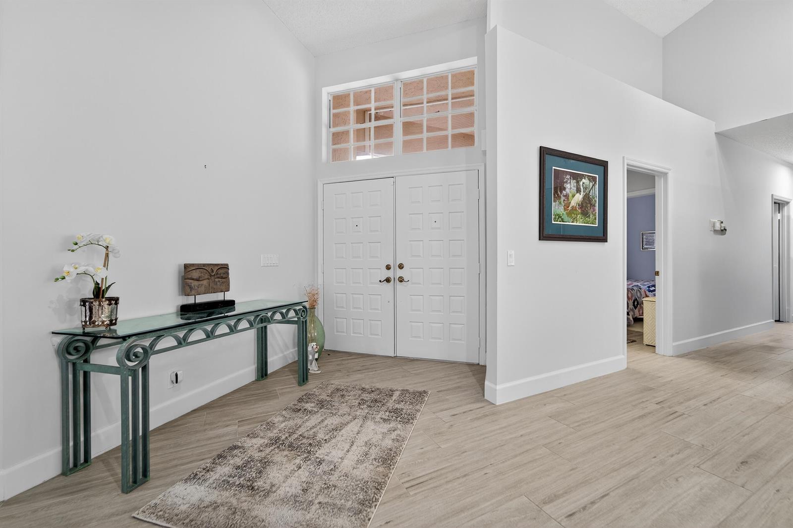 An entryway features a glass console table, double doors, and light-colored wood-look tile flooring — 12902 Touchstone Place, Palm Beach Gardens FL 33418, PALM BEACH GARDENS, FL