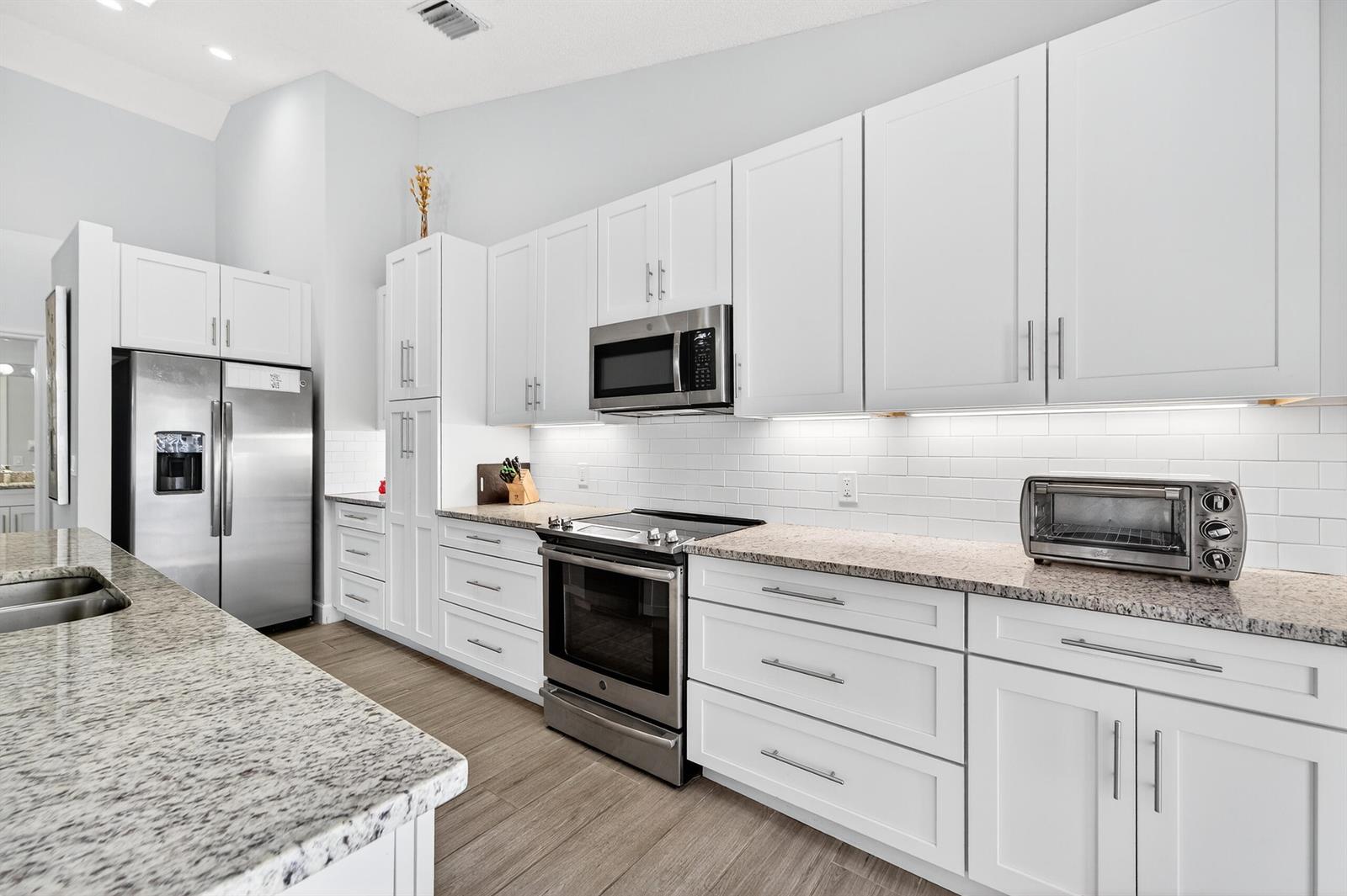 A modern kitchen features white cabinets, stainless steel appliances, granite countertops, and a subway tile backsplash — 12902 Touchstone Place, Palm Beach Gardens FL 33418, PALM BEACH GARDENS, FL