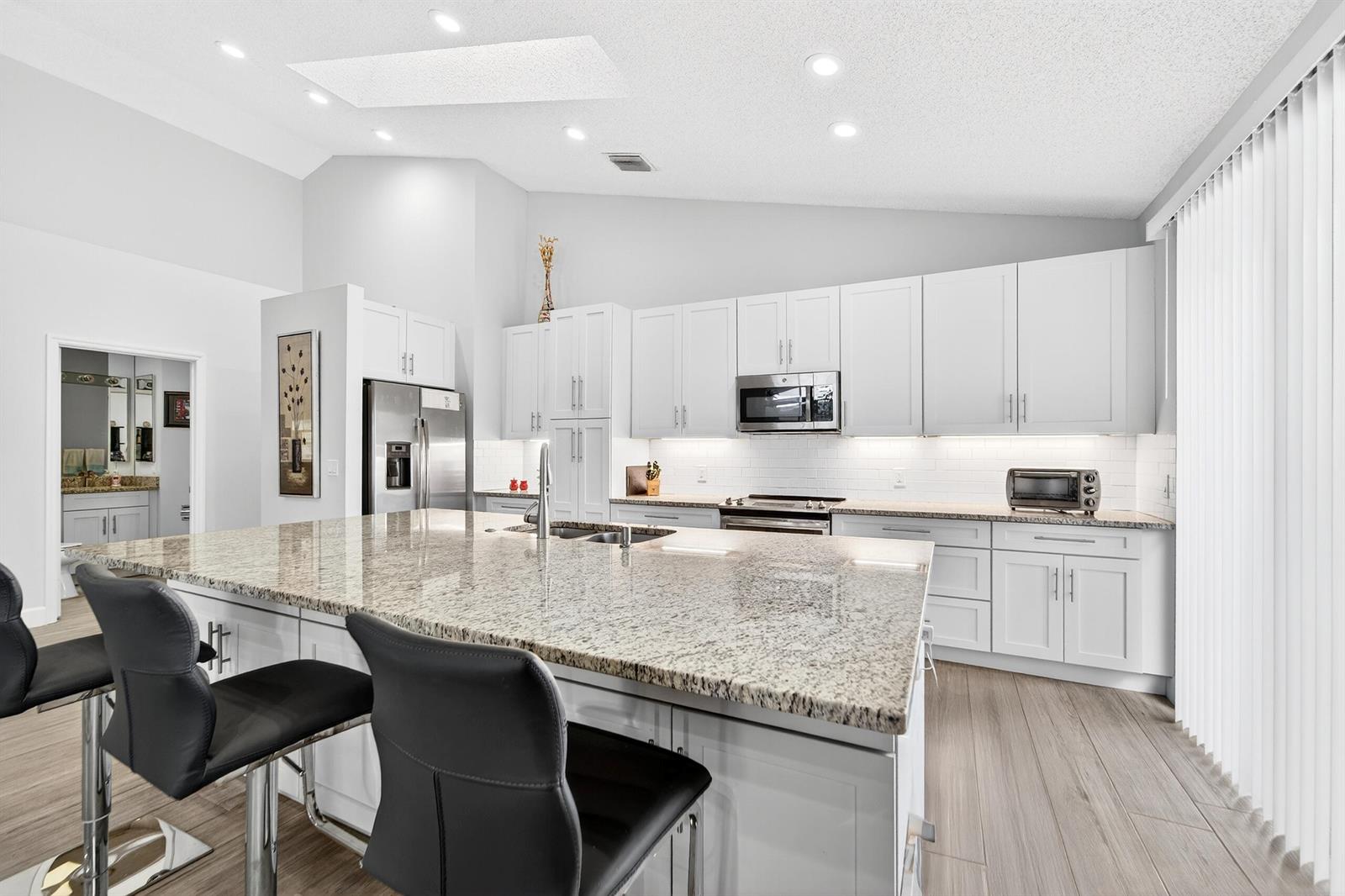 A modern kitchen features white cabinets, granite countertops, a large island, and stainless steel appliances — 12902 Touchstone Place, Palm Beach Gardens FL 33418, PALM BEACH GARDENS, FL
