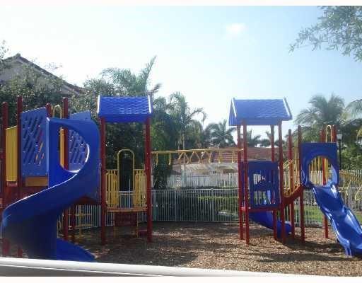 A colorful outdoor playground structure with slides and monkey bars sits on a wood-chipped surface — 3936 San Simeon Lane # 3936, Weston FL 33331, WESTON, FL