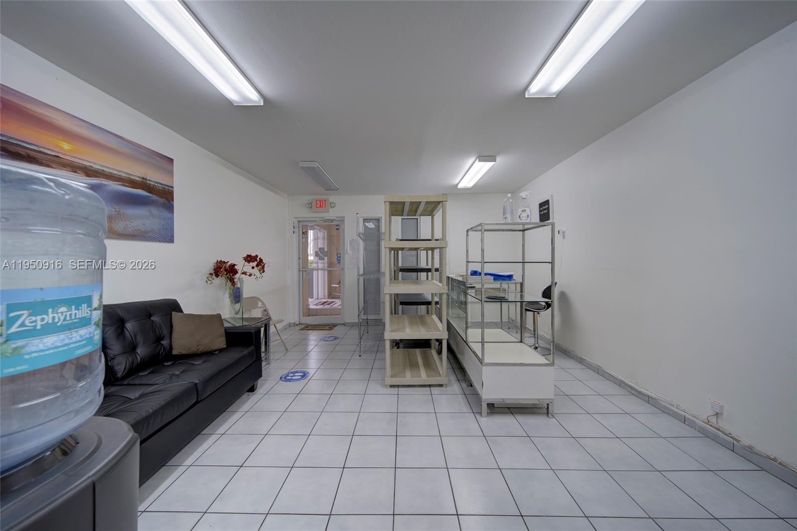 A commercial room features white tile floors, a black sofa, shelving units, and fluorescent lighting — 330 W 9th St, Hialeah FL 33010, HIALEAH, FL