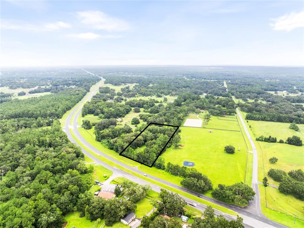 An aerial view shows a rectangular wooded lot outlined in black next to a highway — 12255 N US HIGHWAY 27, OCALA, FL
