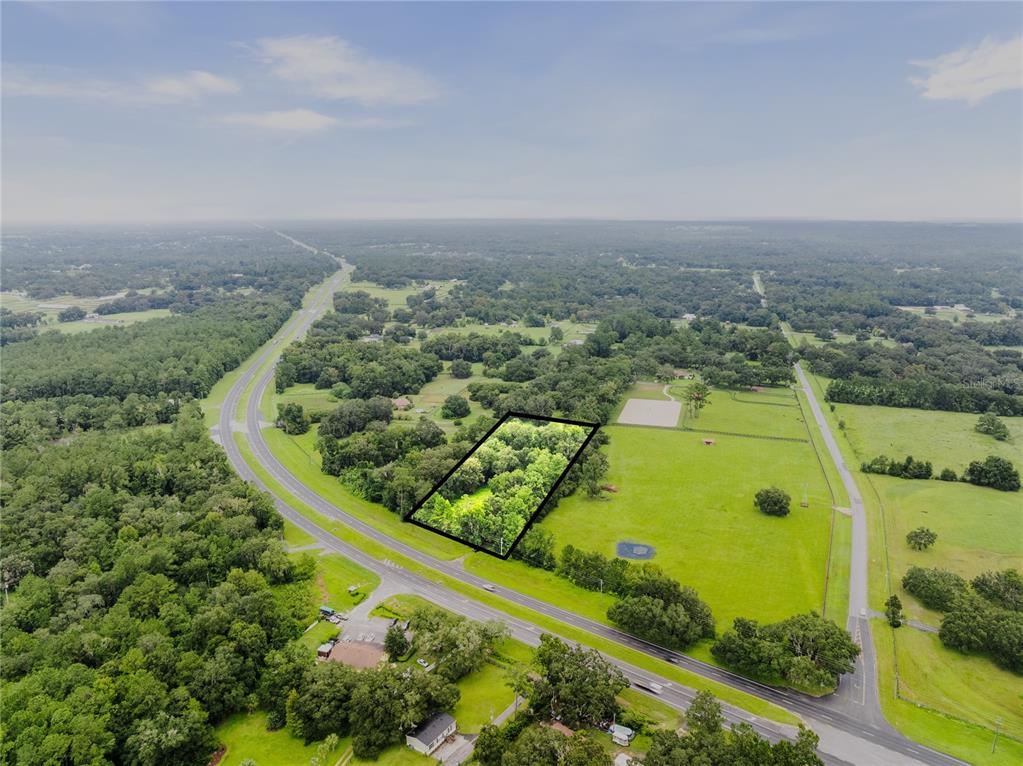 An aerial view shows a rectangular wooded lot outlined in black next to a highway — 12255 N US HIGHWAY 27, OCALA, FL