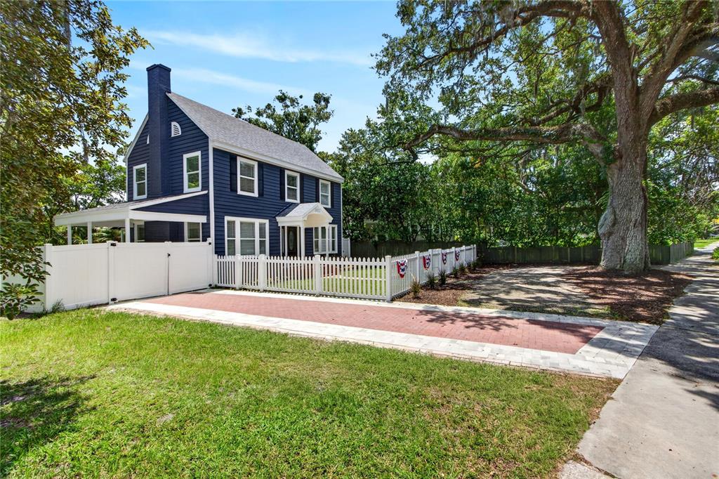 A two-story dark blue house features a white picket fence and a brick driveway — 1811 SANFORD AVENUE, SANFORD, FL