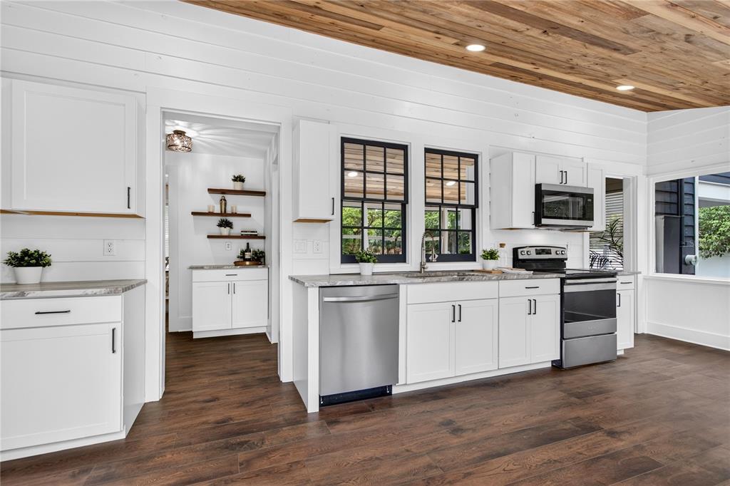 A kitchen features white cabinets, stainless steel appliances, dark wood flooring, and a wood-paneled ceiling — 1811 SANFORD AVENUE, SANFORD, FL