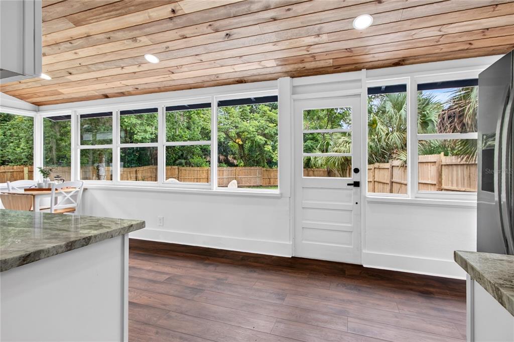 A sunroom with wood-plank ceiling, dark wood-look flooring, white trim, and large windows — 1811 SANFORD AVENUE, SANFORD, FL