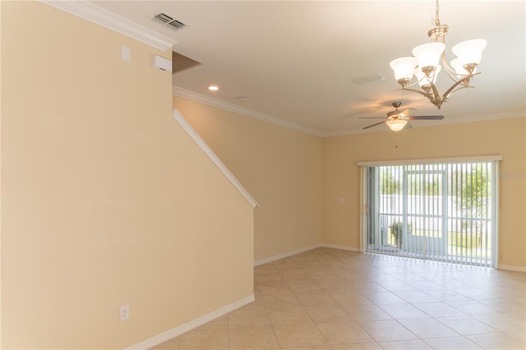 An empty living room features tile flooring, a ceiling fan, a chandelier, and sliding glass doors — 31235 CLARIDGE PLACE, WESLEY CHAPEL, FL
