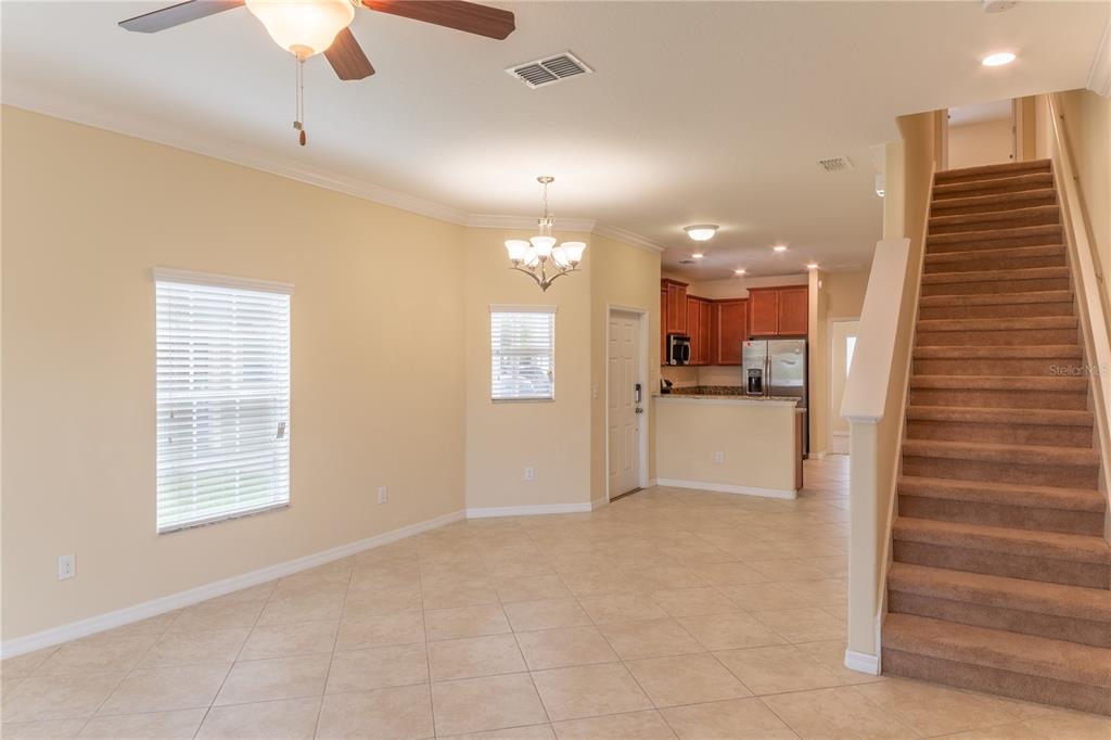 An open-concept living area with tile flooring, a carpeted staircase, and an adjacent kitchen — 31235 CLARIDGE PLACE, WESLEY CHAPEL, FL