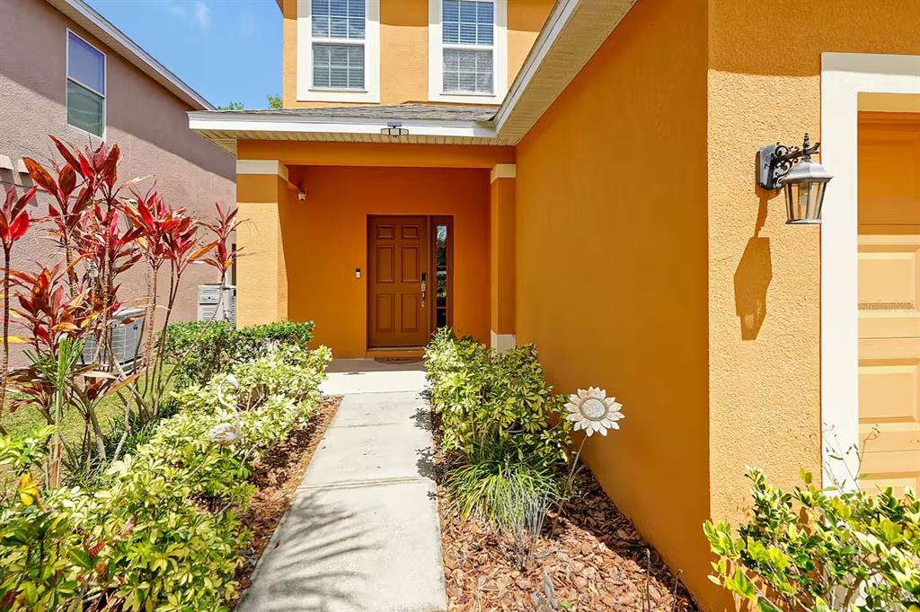 A concrete walkway leads to the front entrance of a house with orange stucco walls — 2650 SANTOSH COVE, KISSIMMEE, FL