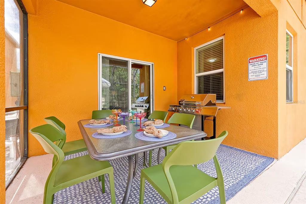 A covered patio features a dining table with green chairs, a grill, and orange walls — 2650 SANTOSH COVE, KISSIMMEE, FL