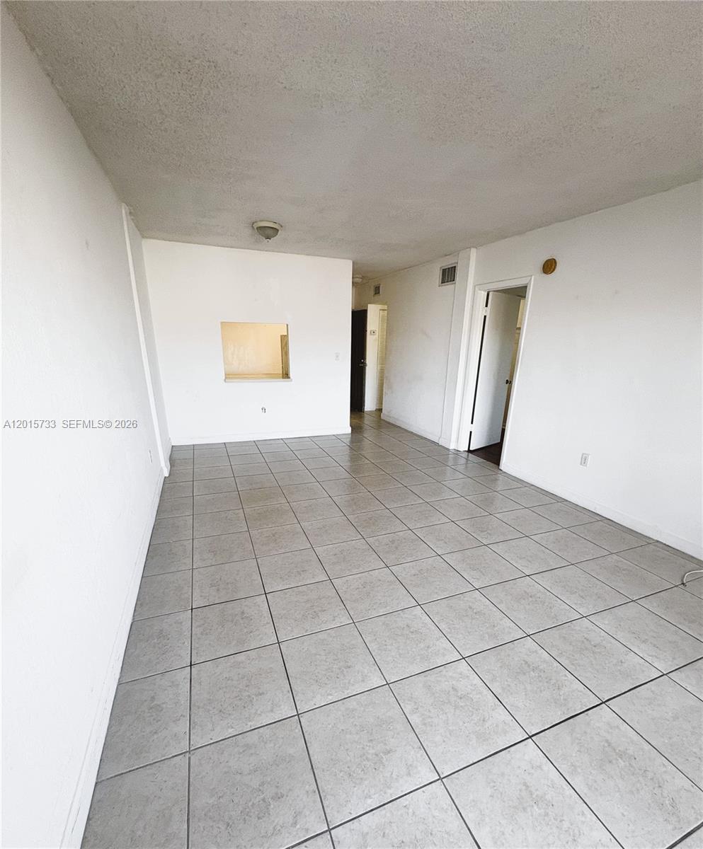 An empty room features white walls, gray tile flooring, and a small kitchen pass-through window — 10900 SW 104th St # 315, Miami FL 33176, MIAMI, FL