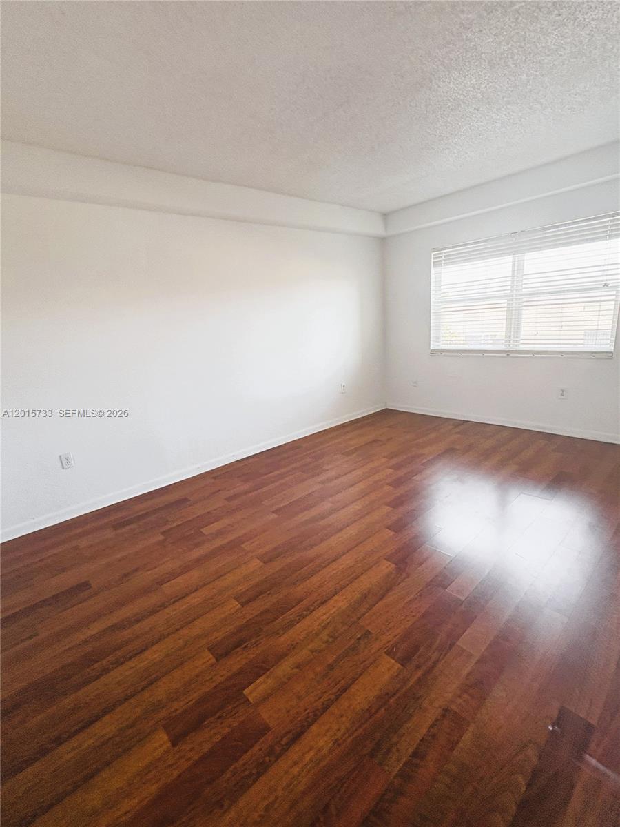 An empty room features white walls, a single window with blinds, and dark wood flooring — 10900 SW 104th St # 315, Miami FL 33176, MIAMI, FL