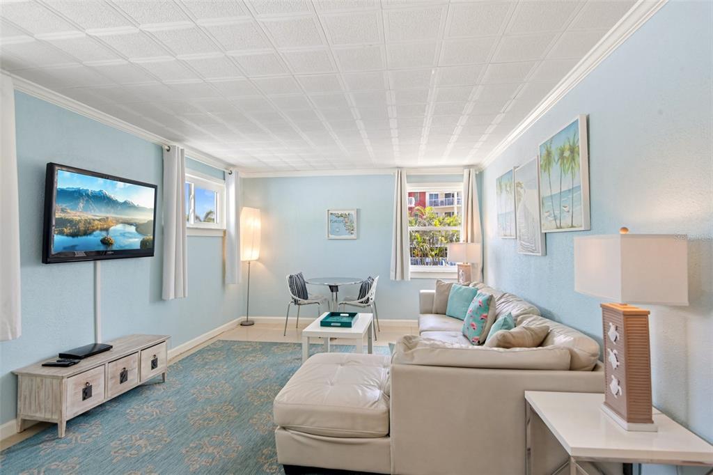 A living room with light blue walls, a sectional sofa, a television, and a dining area — 11730 GULF BOULEVARD UNIT 40, ST PETERSBURG, FL