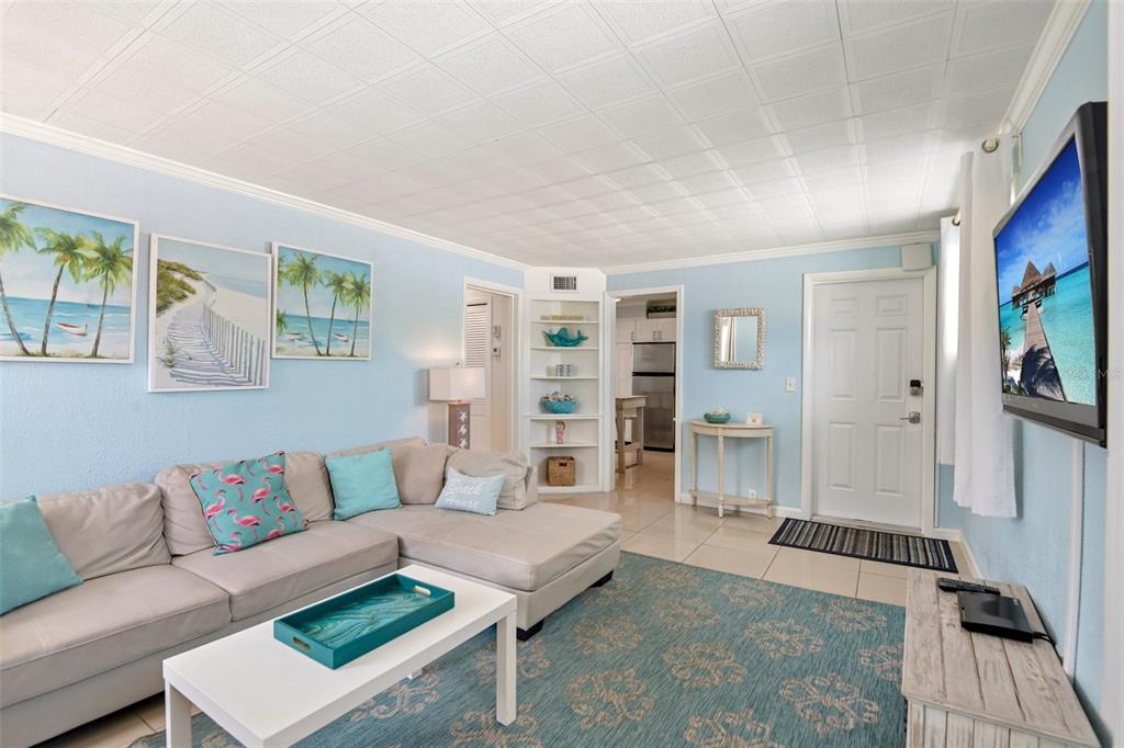 A living room features light blue walls, a sectional sofa, a rug, and a television — 11730 GULF BOULEVARD UNIT 40, ST PETERSBURG, FL