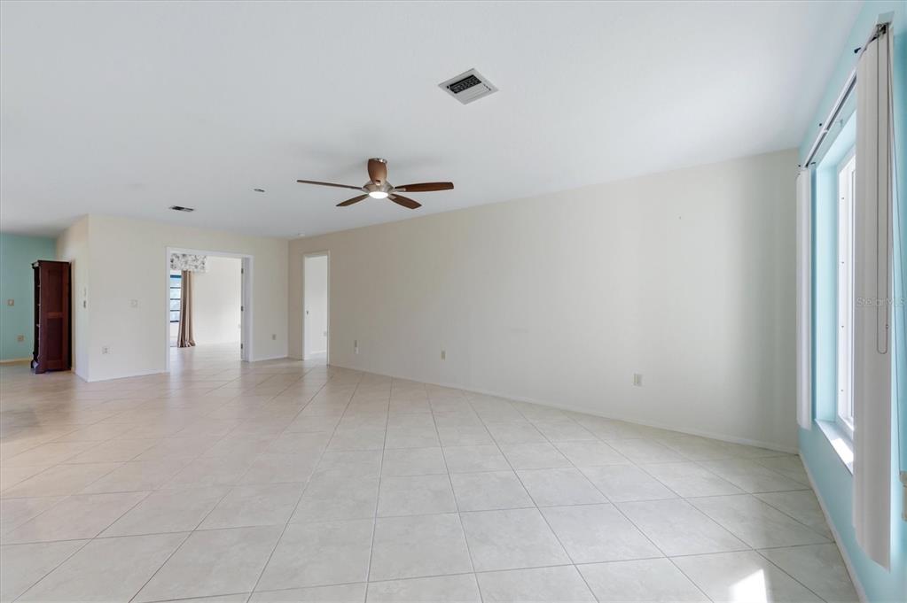 A spacious, empty living room features light-colored tile flooring, white walls, and a ceiling fan — 255 RIGEL ROAD, VENICE, FL