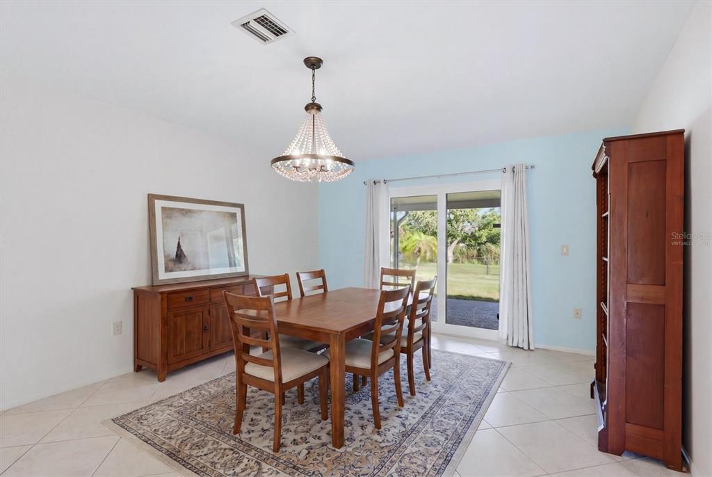 A dining room features a wooden table, chairs, a sideboard, and a chandelier on tile — 255 RIGEL ROAD, VENICE, FL