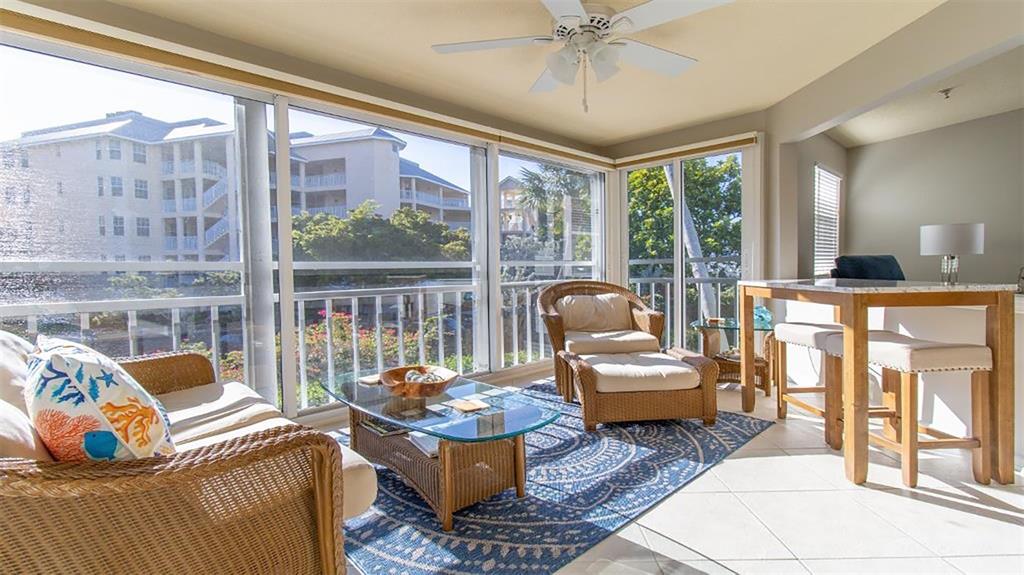 A sunroom features wicker furniture, a glass coffee table, and a blue patterned area rug — 1340 SIESTA BAYSIDE DRIVE UNIT 1340-C, SARASOTA, FL