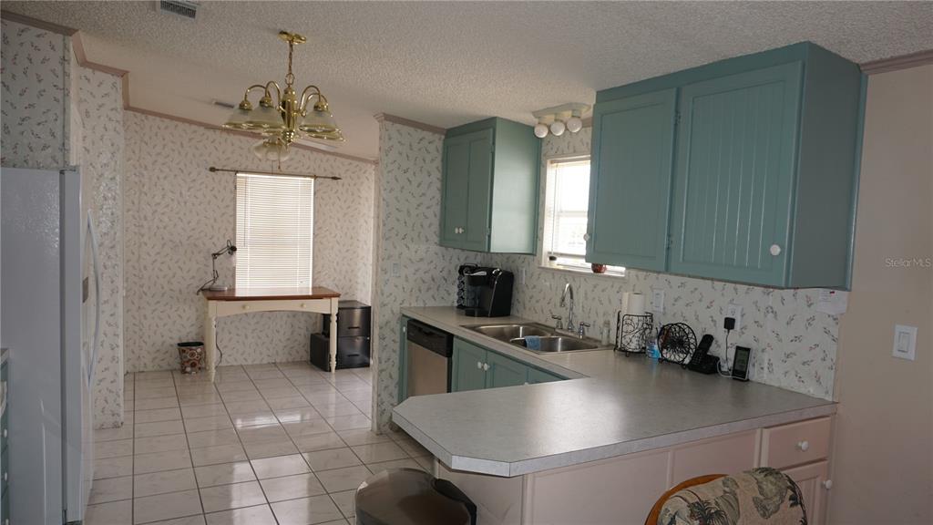 A kitchen features teal upper cabinets, light-colored countertops, tiled flooring, and a dining area — 12023 LONGHORN DRIVE, HUDSON, FL