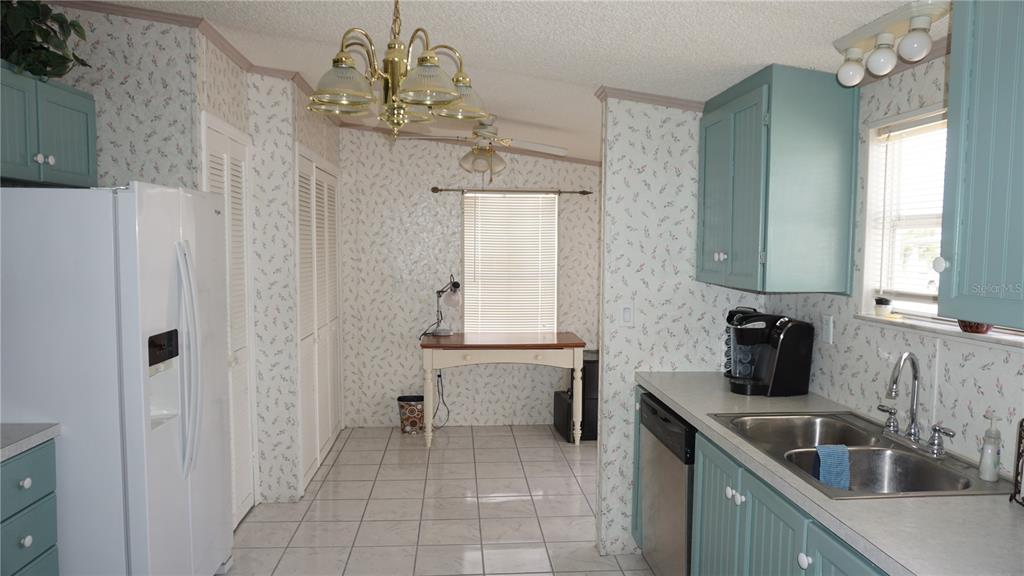 A kitchen with light blue cabinets, floral wallpaper, white appliances, and a small wooden table — 12023 LONGHORN DRIVE, HUDSON, FL
