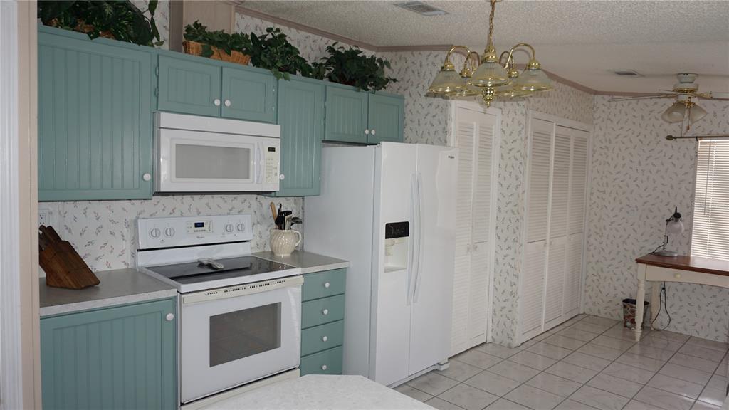 A kitchen features teal cabinets, white appliances, patterned wallpaper, and a dining area — 12023 LONGHORN DRIVE, HUDSON, FL